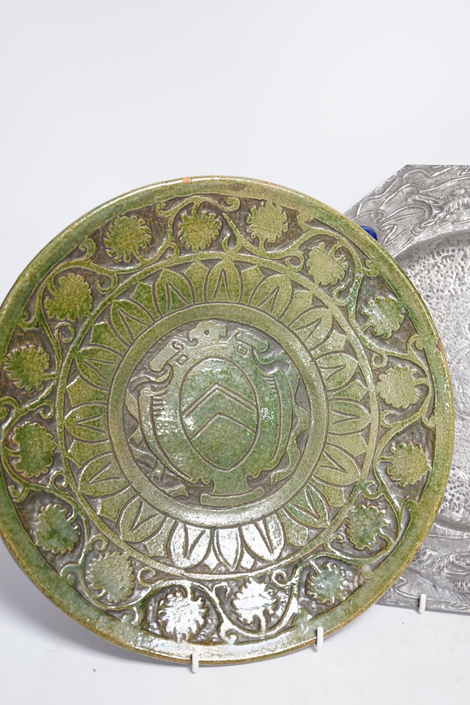 An Arts and Crafts style pewter fish plate with ceramic insets and glass eyes together with a pottery armorial charger, pewter charger 35cm wide